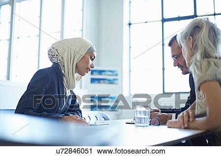 Stock Image - Two businesswomen and man looking at digital tablet in office meeting. Fotosearch