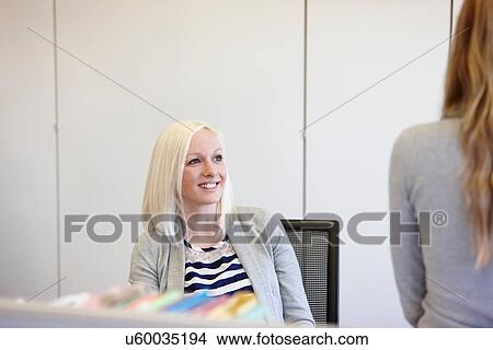 Picture - Two businesswomen chatting at desk in office. Fotosearch