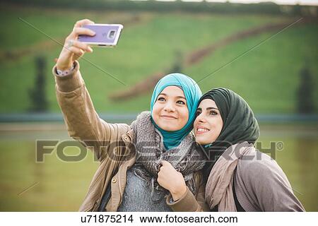 Two female friends at lakeside posing for smartphone selfie View Large Photo Image Picture - Two female friends at lakeside posing for smartphone selfie. Fotosearch