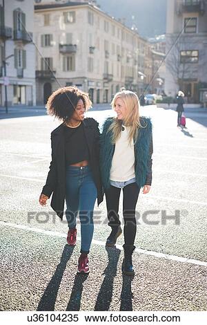 Stock Photography - Two female friends chatting and strolling in town square. Fotosearch