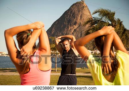 Stock Photo - "Two female friends exercising in park with personal trainer, Rio De Janeiro, Brazil". Fotosearch