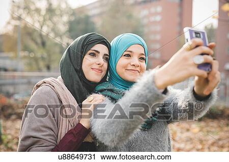 Stock Image - Two female friends in park posing for smartphone selfie. Fotosearch