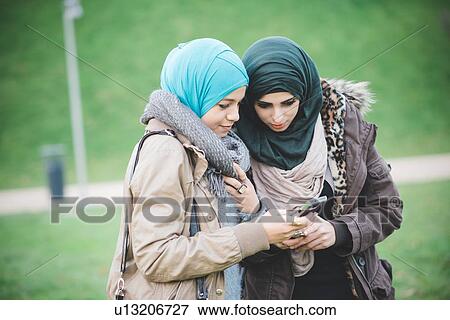 Two female friends in park reading text on smartphones View Large Photo Image Stock Photo - Two female friends in park reading text on smartphones. Fotosearch