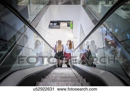 Two female friends moving up escalator in shopping mall View Large Photo Image Stock Image - Two female friends moving up escalator in shopping mall. Fotosearch