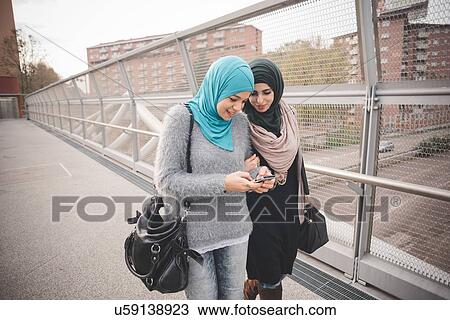 Stock Image - Two female friends on footbridge reading smartphone texts. Fotosearch