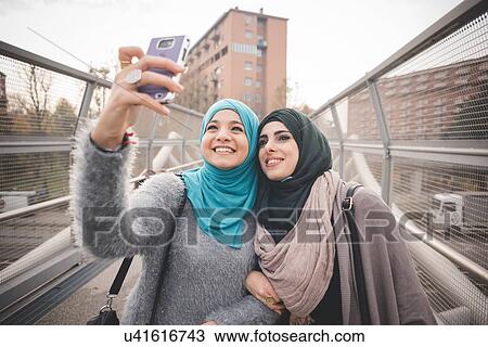 Two female friends on footbridge taking smartphone selfie View Large Photo Image Stock Image - Two female friends on footbridge taking smartphone selfie. Fotosearch
