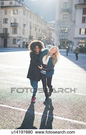 Two female friends walking and laughing in town square View Large Photo Image Stock Image - Two female friends walking and laughing in town square. Fotosearch