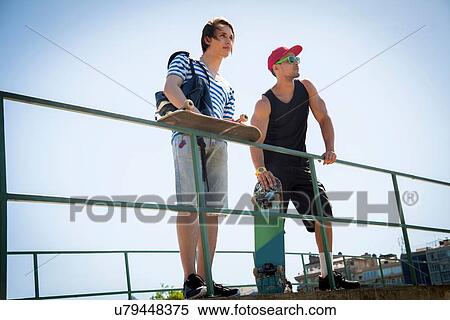"Two men, holding skateboards, leaning on railings" View Large Photo Image Stock Photography - "Two men, holding skateboards, leaning on railings". Fotosearch