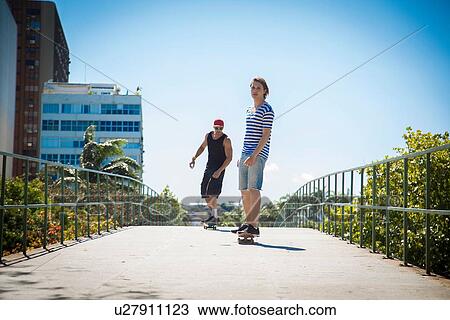 "Two men skateboarding along walkway, low angle view" View Large Photo Image Stock Image - "Two men skateboarding along walkway, low angle view". Fotosearch