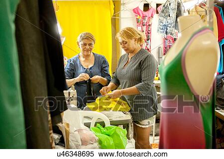 Stock Photography - Two seamstresses preparing garments for sewing in workshop. Fotosearch