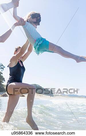 "Two women lifting girl over ocean waves, Hot Water Beach, Bay of Islands, New Zealand" View Large Photo Image Stock Photograph - "Two women lifting girl over ocean waves, Hot Water Beach, Bay of Islands, New Zealand". Fotosearch