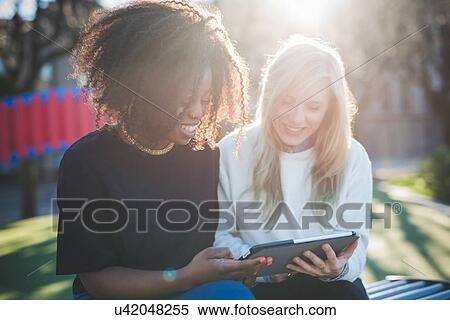 "Two young female friends on park bench looking at digital tablet, Como, Italy" View Large Photo Image Stock Photography - "Two young female friends on park bench looking at digital tablet, Como, Italy". Fotosearch