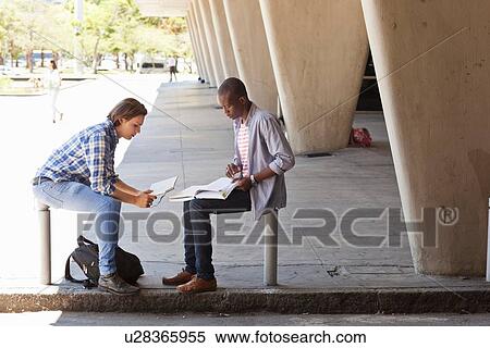 Two young men sitting outside building studying View Large Photo Image Stock Photography - Two young men sitting outside building studying. Fotosearch