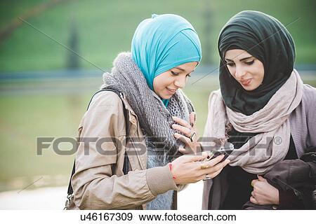Two young women at lakeside texting on smartphone View Large Photo Image Stock Photo - Two young women at lakeside texting on smartphone. Fotosearch