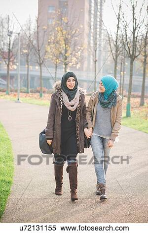 Stock Photography - Two young women chatting whilst strolling in park. Fotosearch