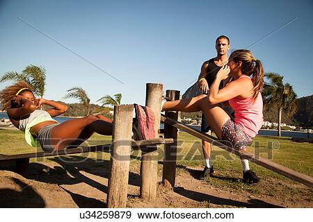 Two young women doing sit ups on wooden workbench in park View Large Photo Image Stock Photo - Two young women doing sit ups on wooden workbench in park. Fotosearch