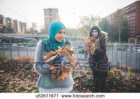 Two young women friends collecting autumn leaves in park View Large Photo Image Stock Image - Two young women friends collecting autumn leaves in park. Fotosearch