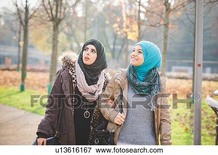 Stock Photo - Two young women looking up whilst strolling in park. Fotosearch