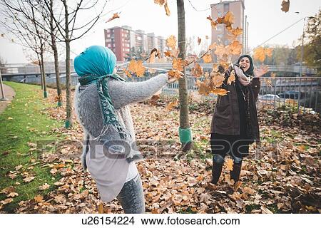 Two young women play fighting with autumn leaves in park View Large Photo Image Picture - Two young women play fighting with autumn leaves in park. Fotosearch