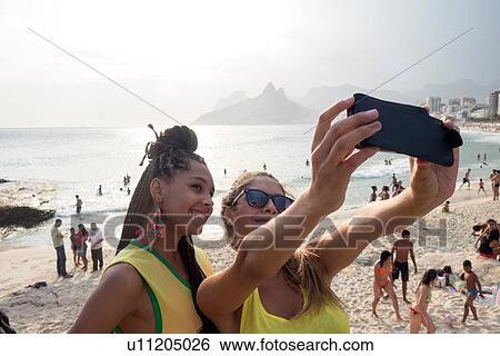 "Two young women taking smartphone selfie on Ipanema beach, Rio De Janeiro, Brazil" View Large Photo Image Stock Photograph - "Two young women taking smartphone selfie on Ipanema beach, Rio De Janeiro, Brazil". Fotosearch