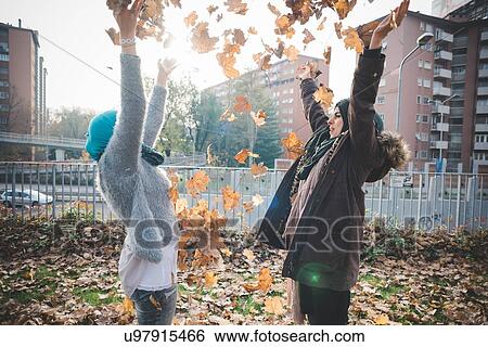 Stock Photograph - Two young women throwing autumn leaves in park. Fotosearch