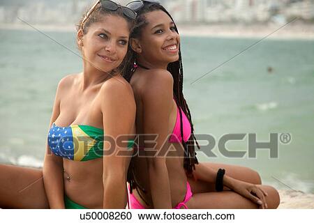 "Two young women wearing bikinis sitting back to back on Ipanema beach, Rio De Janeiro, Brazil" View Large Photo Image Stock Image - "Two young women wearing bikinis sitting back to back on Ipanema beach, Rio De Janeiro, Brazil". Fotosearch