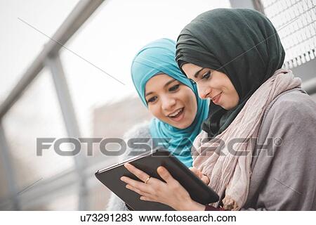 Two young women wearing hijabs using digital tablet on footbridge View Large Photo Image Stock Image - Two young women wearing hijabs using digital tablet on footbridge. Fotosearch