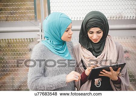 Two young women wearing hijabs using touchscreen on digital tablet on footbridge View Large Photo Image Stock Photo - Two young women wearing hijabs using touchscreen on digital tablet on footbridge. Fotosearch