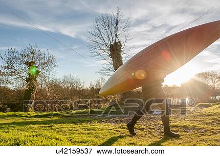 Stock Photo - Woman carrying canoe in field. Fotosearch