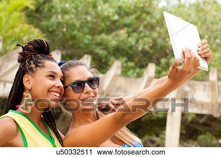 Stock Image - "Women taking selfie using digital tablet, Rio de Janeiro, Brazil". Fotosearch