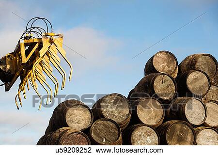 Stock Image - Wooden whisky casks and grapple loader. Fotosearch