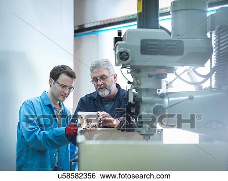 Stock Photograph - Worker and apprentice looking at part in engineering factory. Fotosearch