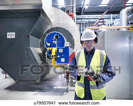 Stock Image - Worker checking readings on digital tablet in gas fired power station. Fotosearch
