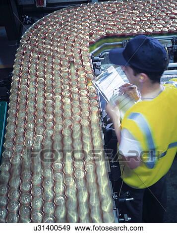 Stock Photo - "Worker inspecting canning line in brewery, high angle view". Fotosearch
