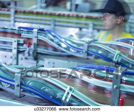 Stock Photograph - Worker inspecting canning line in brewery. Fotosearch