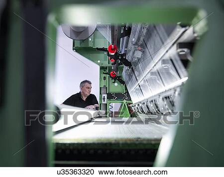 Stock Image - Worker inspecting carbon fibre on loom in carbon fibre factory. Fotosearch