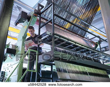 Stock Photo - Worker inspecting carbon fibre on loom in carbon fibre factory. Fotosearch