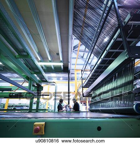 Stock Photograph - Worker inspecting carbon fibre on loom in carbon fibre factory. Fotosearch