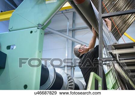 Stock Photo - Worker inspecting carbon fibre thread on loom in carbon fibre factory. Fotosearch