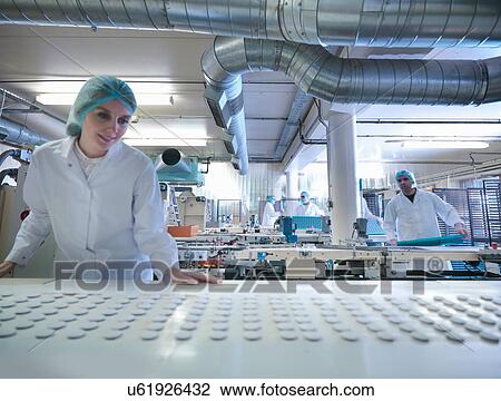 Stock Image - Worker inspecting chocolates on production line in chocolate factory. Fotosearch