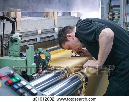 Stock Image - Worker inspecting kevlar fabric in carbon fibre factory. Fotosearch