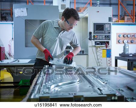 Stock Image - Worker inspecting part of mould in plastics factory. Fotosearch