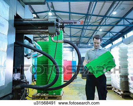Stock Image - Worker inspecting plastic crates in plastics factory. Fotosearch