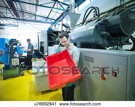 Stock Image - Worker inspecting plastic crates in plastics factory. Fotosearch