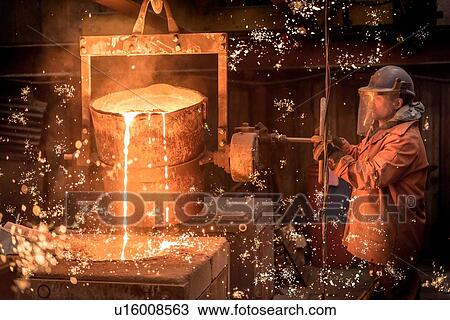 Stock Image - Worker pouring molten metal in foundry. Fotosearch