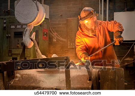 Stock Image - Worker raking molten steel in foundry. Fotosearch