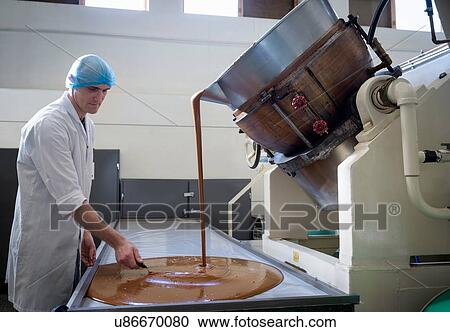 Stock Image - Worker spreading confectionery fudge poured in chocolate factory. Fotosearch
