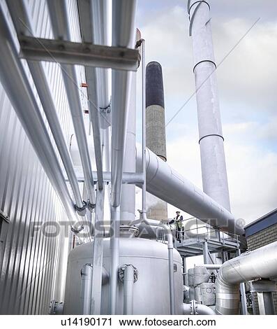 Worker standing amongst pipework of gas fired power station View Large Photo Image Stock Image - Worker standing amongst pipework of gas fired power station. Fotosearch