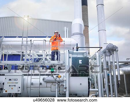 Stock Photo - Worker standing amongst pipework of gas fired power station. Fotosearch
