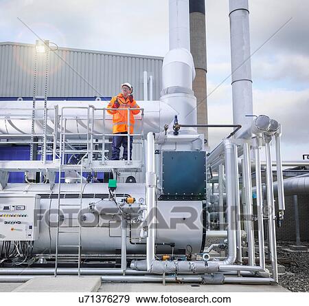 Stock Photo - Worker standing amongst pipework of gas fired power station. Fotosearch